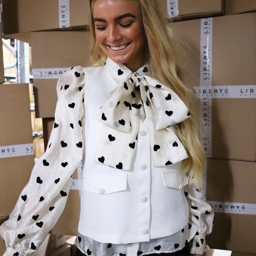 Model fra Liberte Essentiel, står i en skjorte i hvid med sorte hjerter og en Liberte Vest med virkelig flotte glimmer knapper.